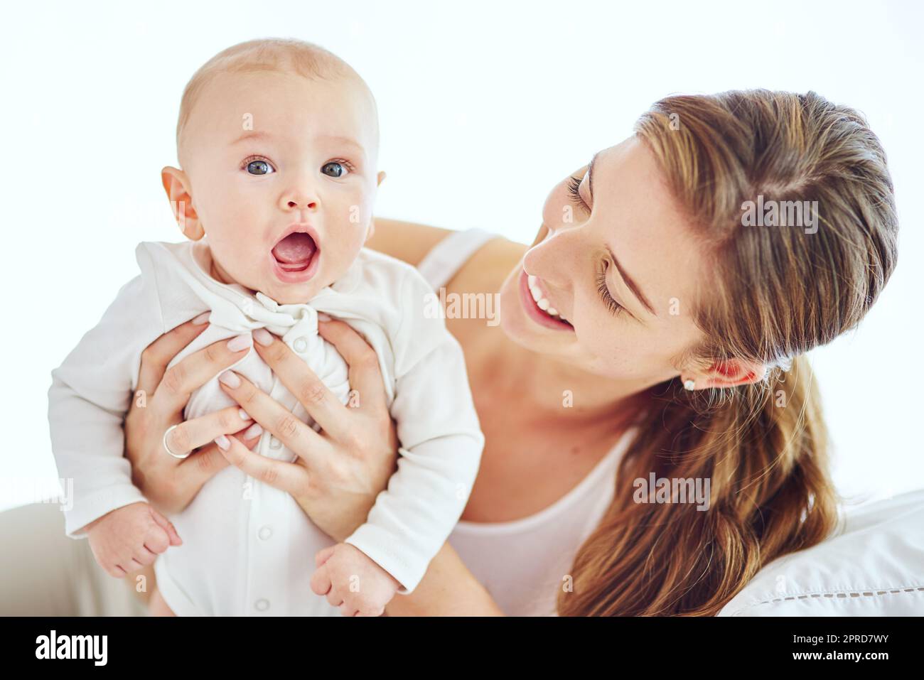 Happy, young and single mother bonding and taking care of adorable baby, enjoying parenthood and being a new mom. Happy female experiencing maternal instinct, holding cute, little child on a bed. Stock Photo
