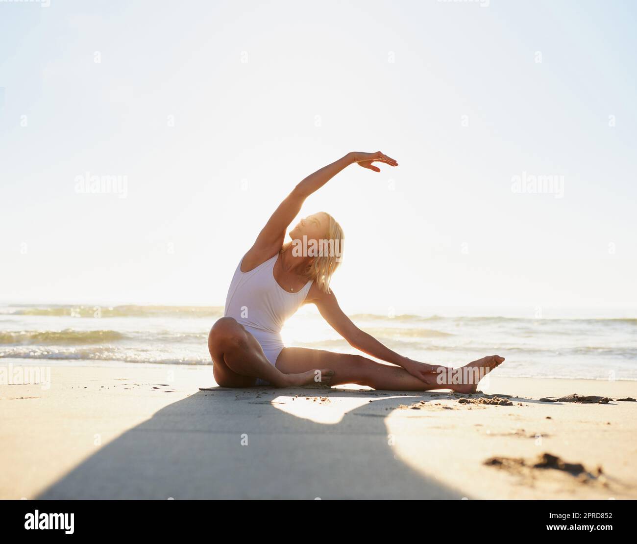 Stretch and hold. Full length shot of an attractive young woman doing a yoga stretch early in the morning on the beach. Stock Photo