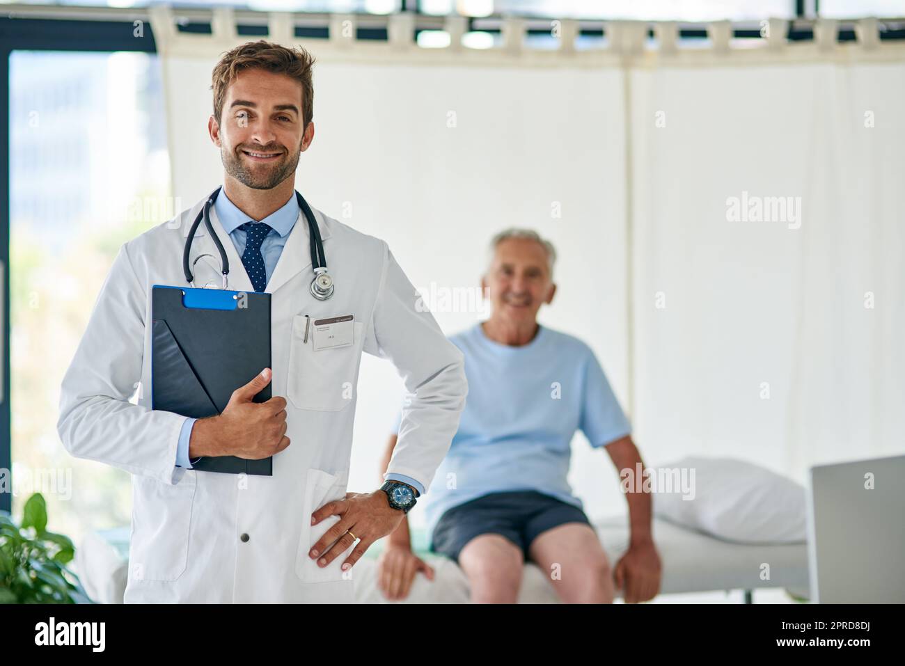 This profession chose me. Cropped portrait of a handsome young doctor standing in his office with an elderly patient in the background. Stock Photo