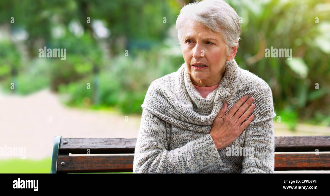 I need to see the doctor again soon. a stressed out elderly woman seated on a bench and holding her chest in discomfort outside in a park. Stock Photo