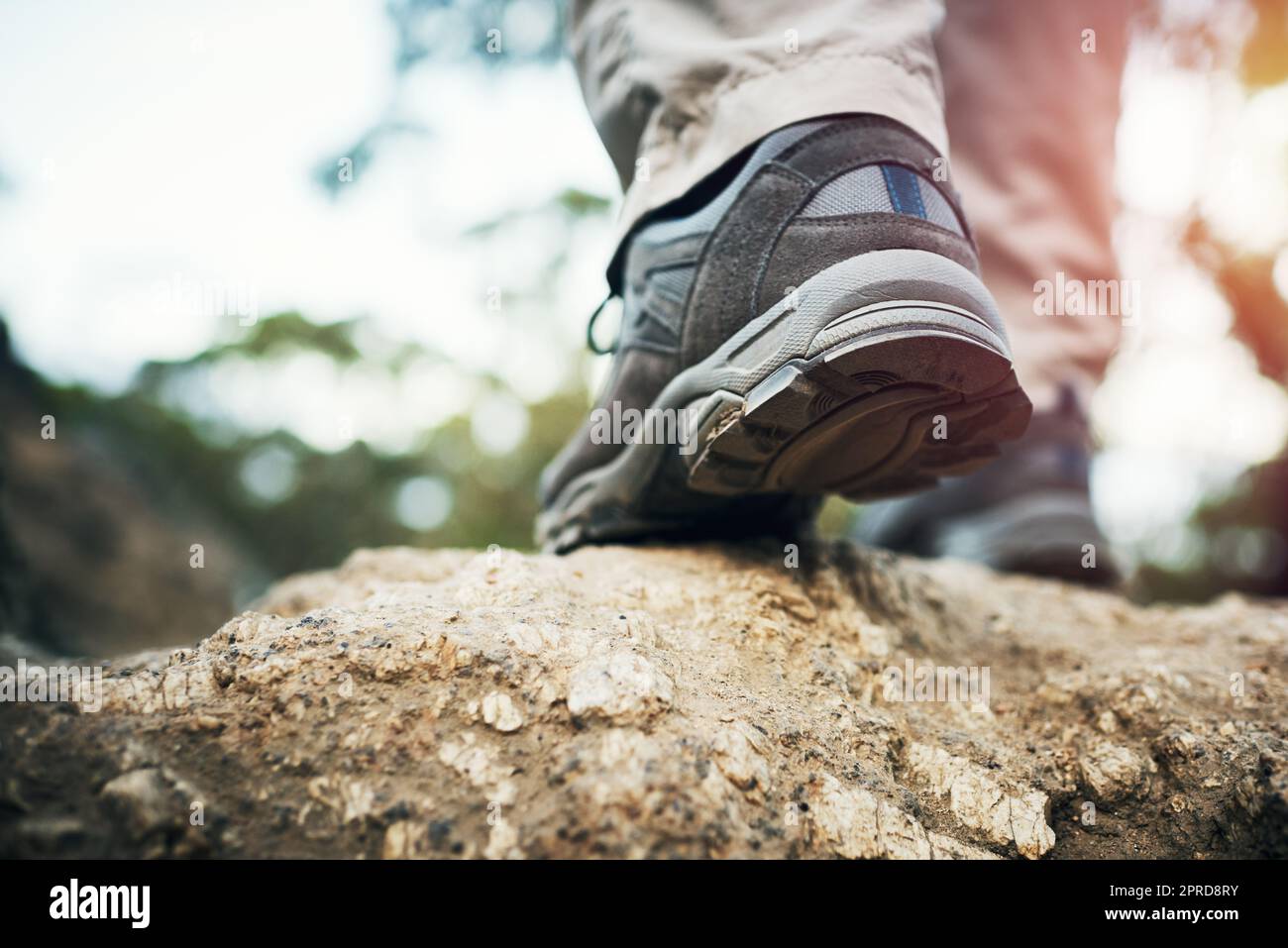 It just takes one step. Low angle shot of an unrecognizable man walking on rocks up a mountain outside during the day. Stock Photo