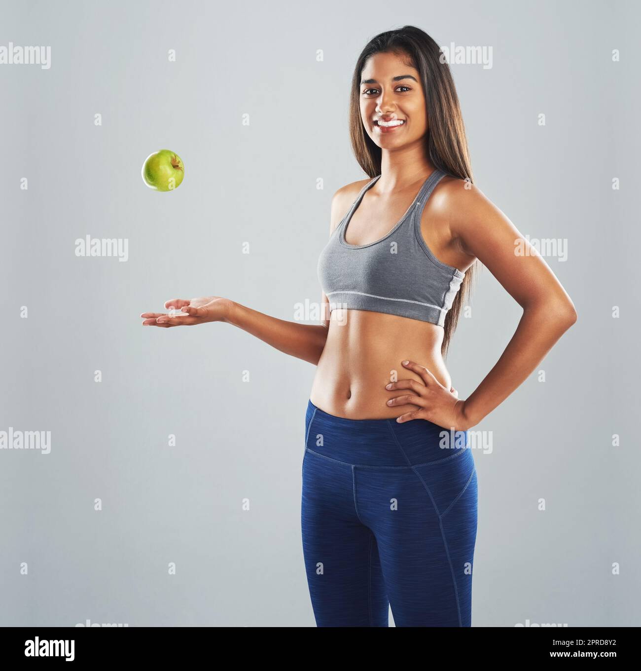 I like to add a little green to my diet. Cropped studio portrait of a happy young woman throwing an apple against a gray background. Stock Photo