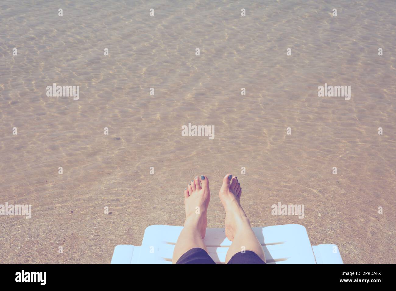 Vacation on tropical beach Woman's legs on the beach bed with clear ocean water background Stock Photo