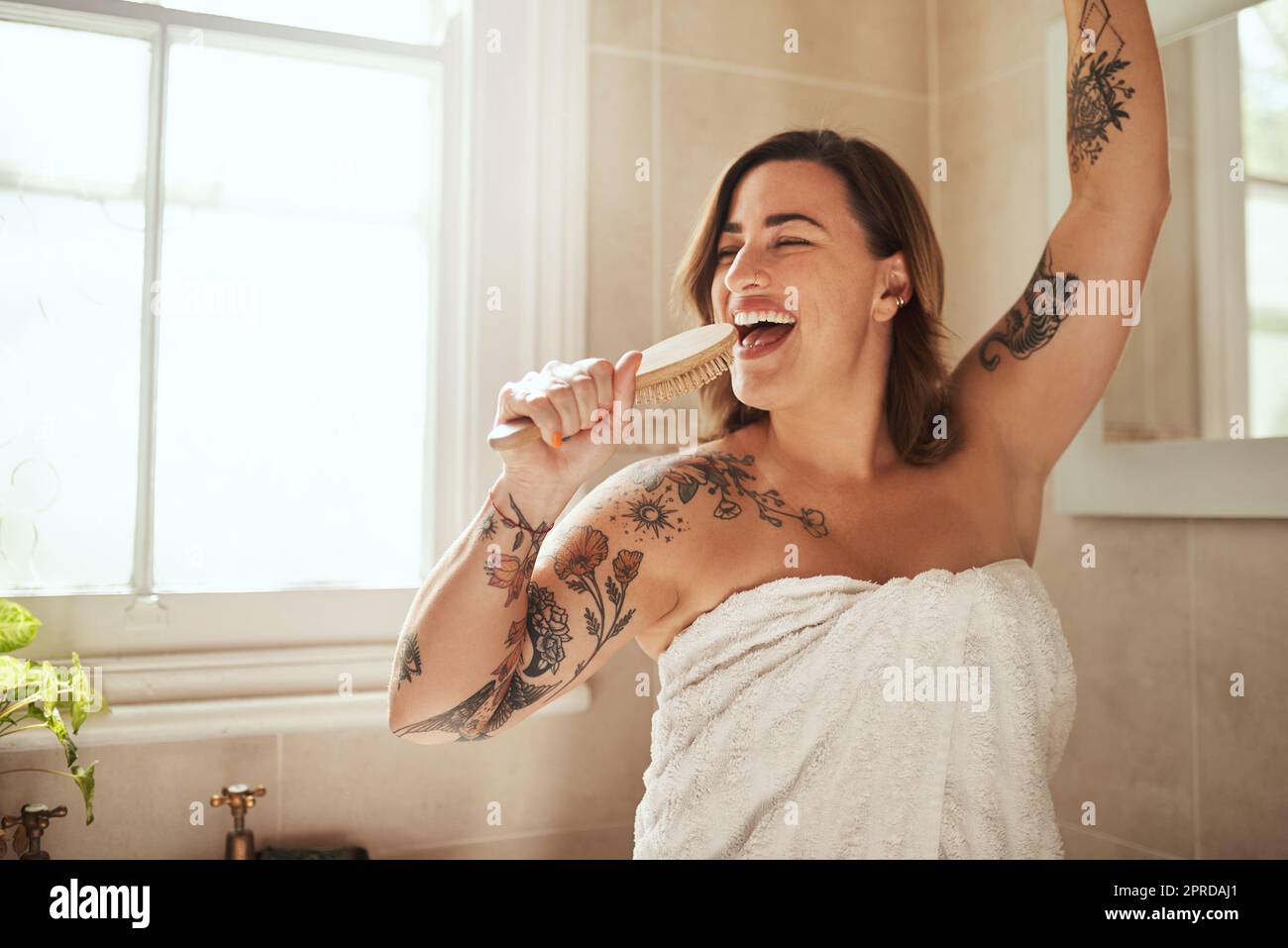 Start off everyday with a song in your heart. an attractive young woman singing while going through her morning beauty routine at home. Stock Photo