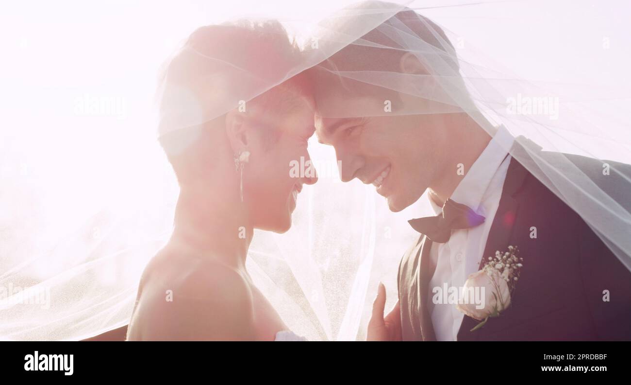 This moment feels so magical. an affectionate young newlywed couple smiling at each other while covering themselves with a veil on their wedding day. Stock Photo