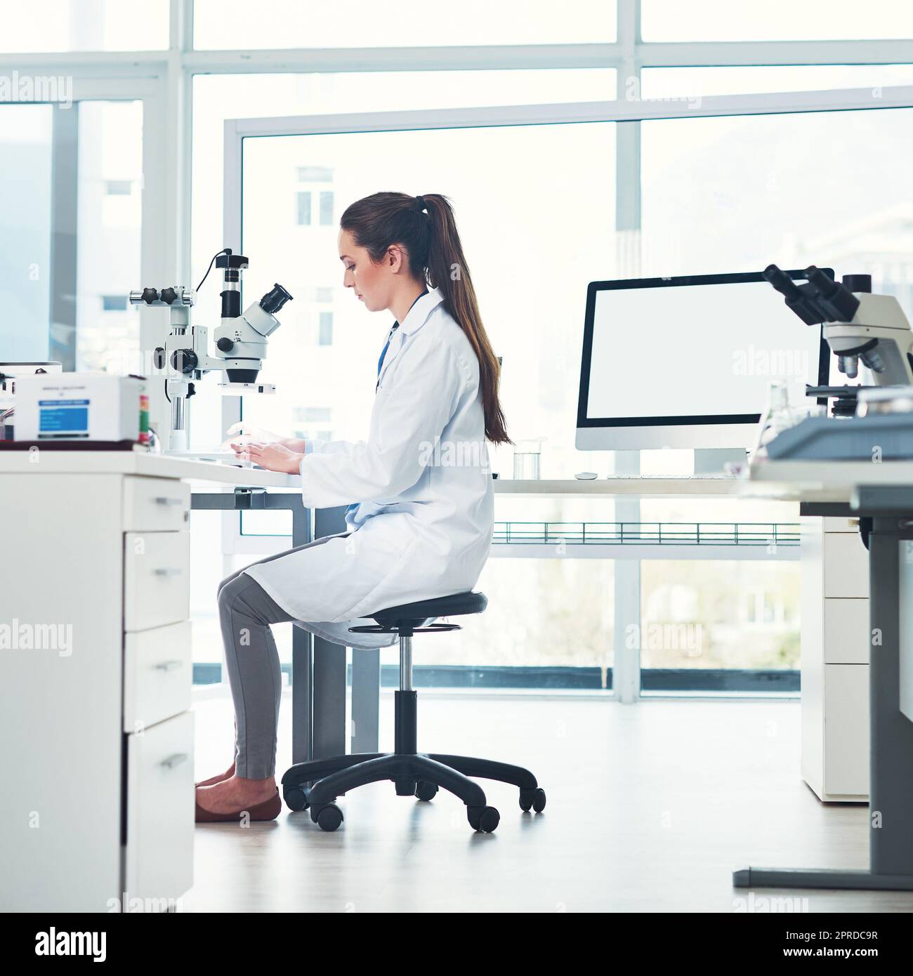 Looking at the new sample. a focused young female scientist conducting experiments inside of a laboratory during the day. Stock Photo