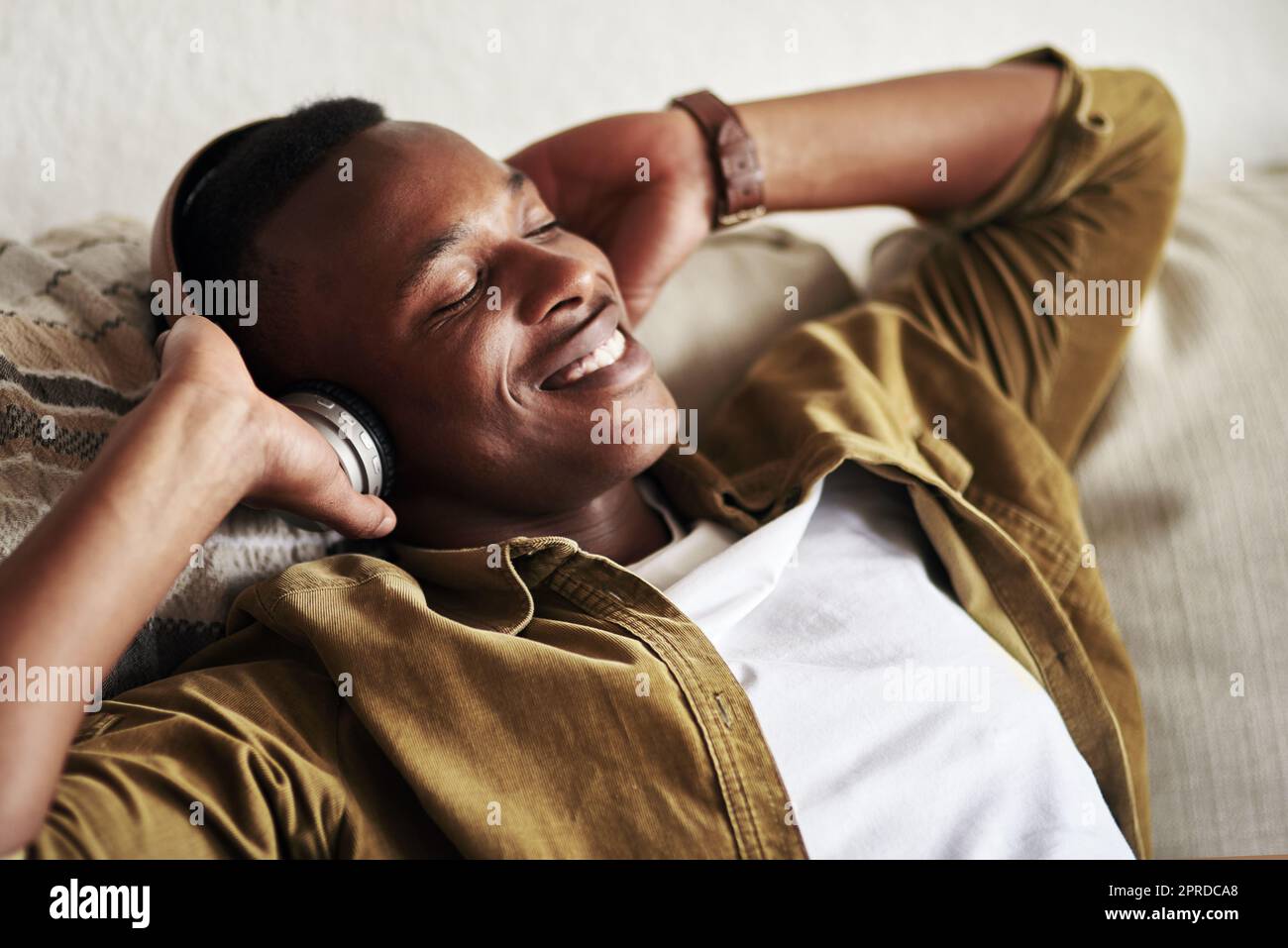 I just love this song. a handsome young man smiling with his eyes closed while listening to music on his headphones at home. Stock Photo