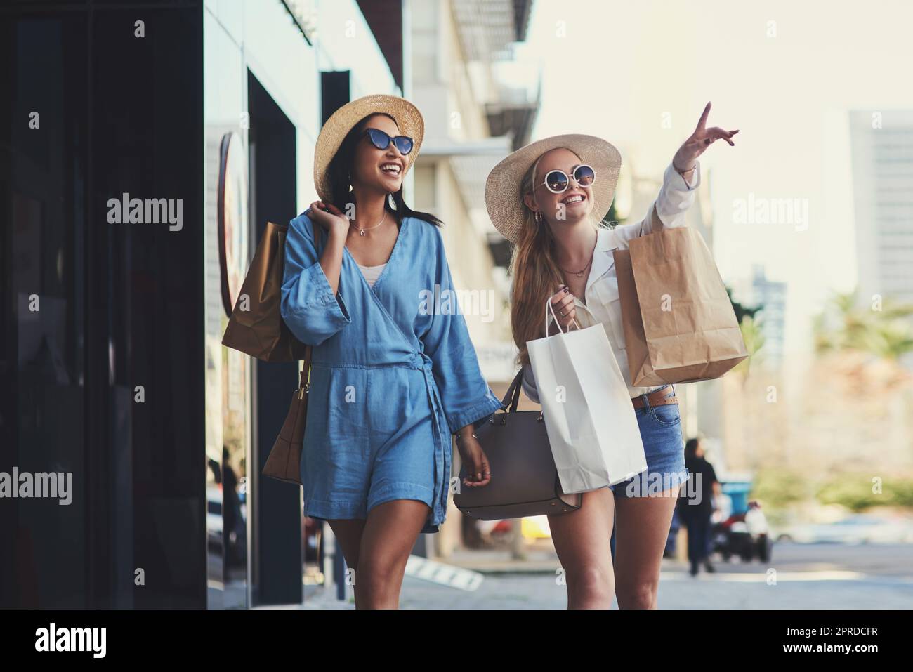We should definitely head to that store. an attractive young woman pointing towards something while walking with her best friend during a shopping spree in the city. Stock Photo