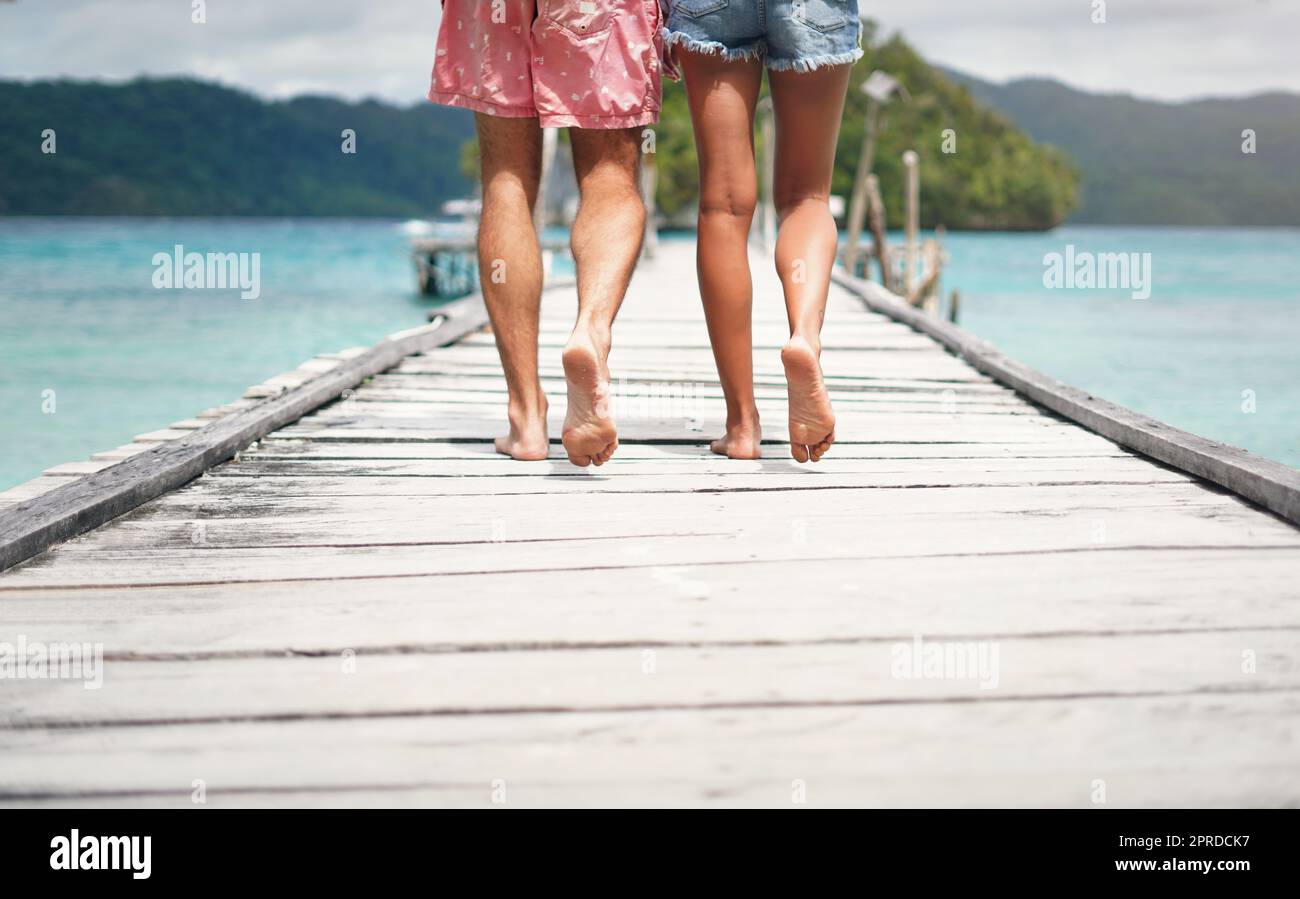 Its just him and I. Rearview shot of an unrecognizable couple walking down a boardwalk overlooking the ocean during a vacation. Stock Photo