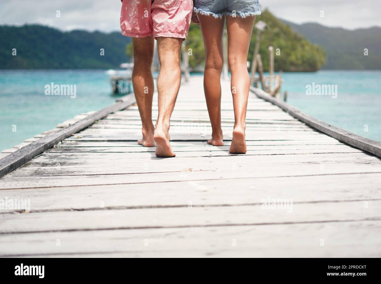 I will go anywhere with him. Rearview shot of an unrecognizable couple walking down a boardwalk overlooking the ocean during a vacation. Stock Photo