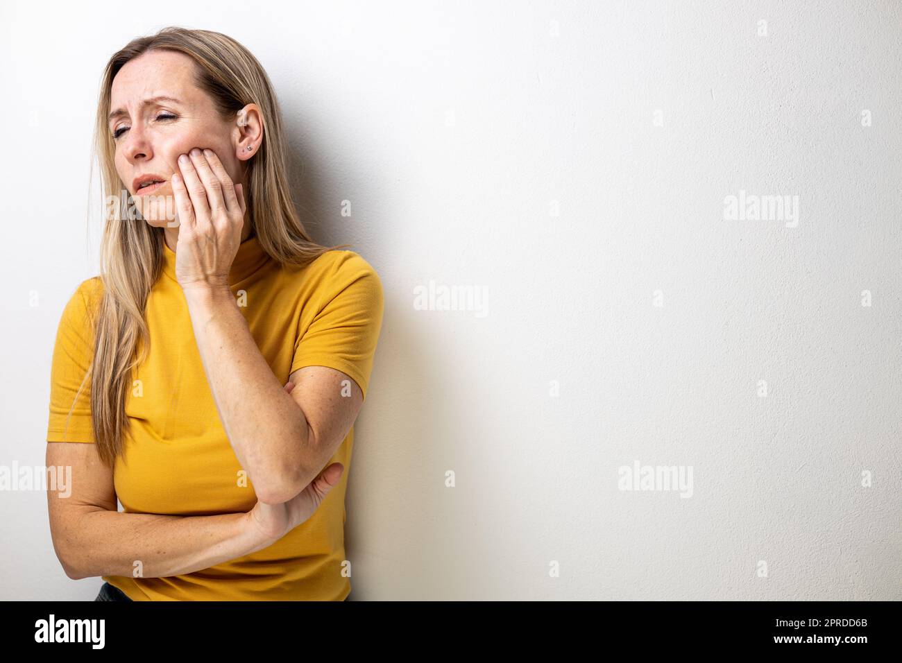 Mid-aged woman touching her cheek/mouth with painful expression because of toothache/dental issue Stock Photo