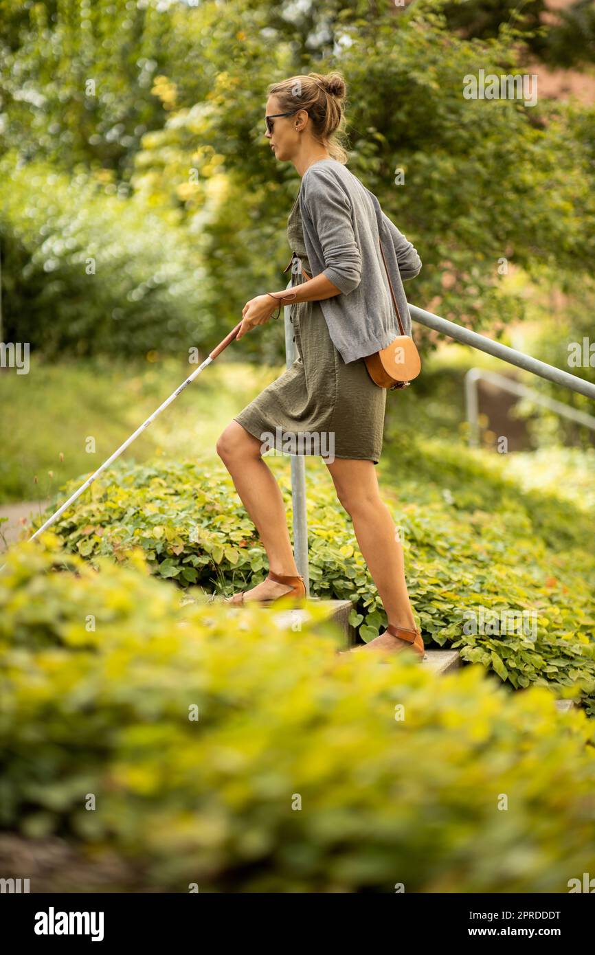 Blind woman walking on city streets, using her white cane to navigate