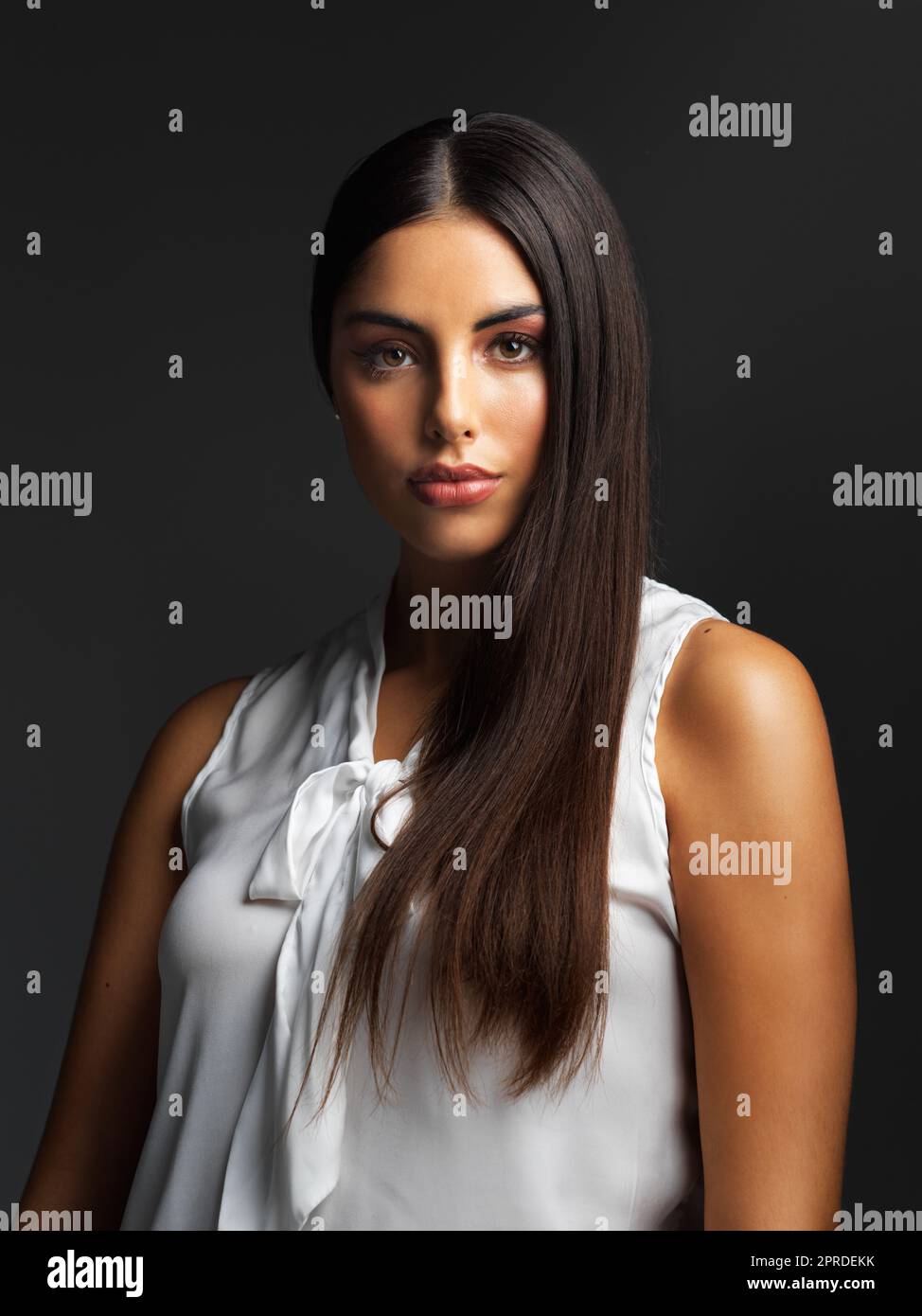 Staring straight into the face of challenges. Portrait of an attractive young woman wearing a white blouse and posing alone against a dark background in the studio. Stock Photo