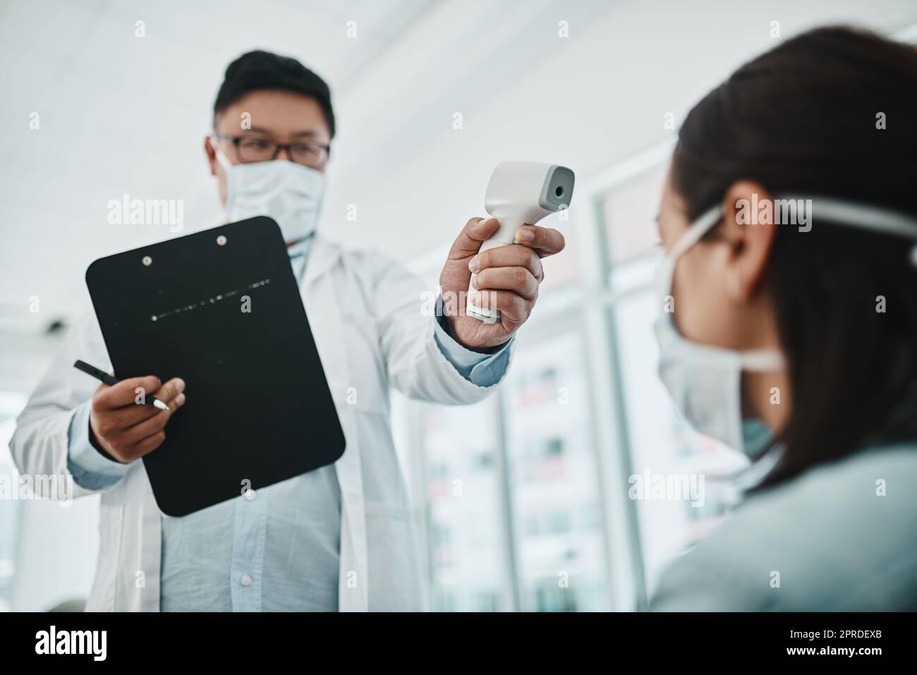 Doctor scanning the temperature of a patient for corona with a digital thermometer. Health care professional consulting with a concerned female about flu symptoms during the covid virus pandemic Stock Photo