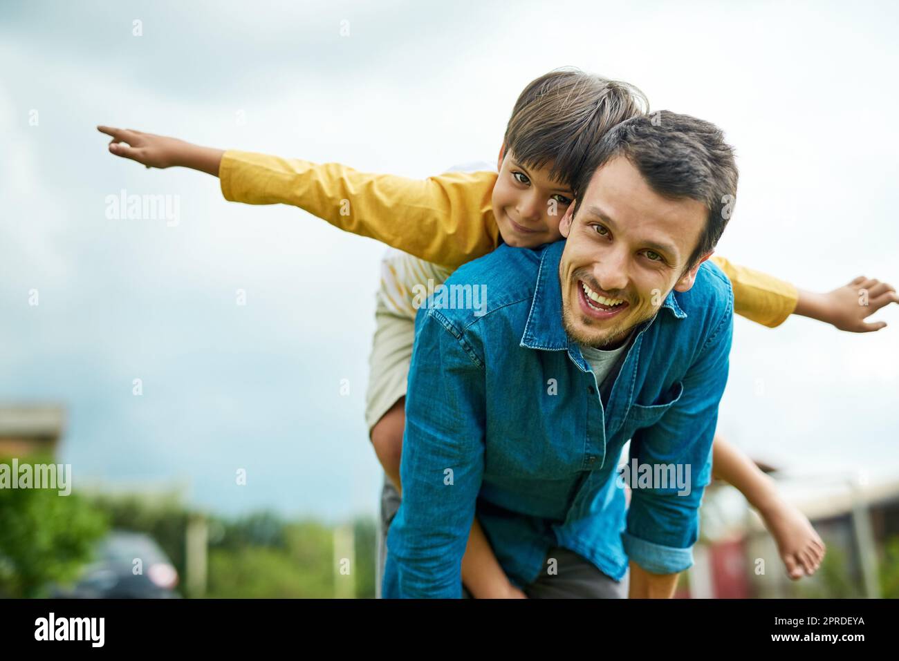 Taking flight with my little man. Portrait of a cheerful young father giving his son a piggyback ride outdoors. Stock Photo