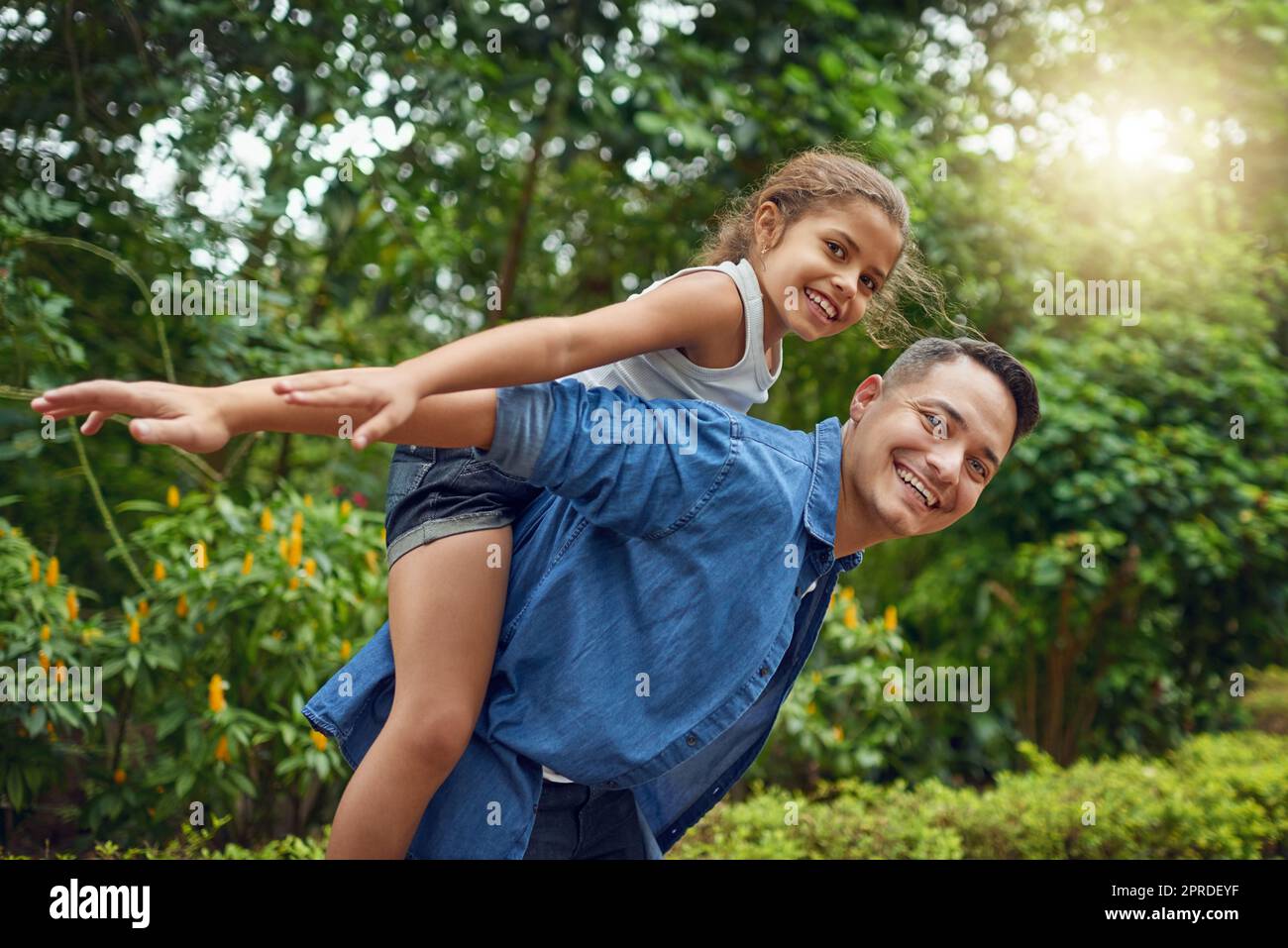 Their bond is as bright as a summers day. Cropped portrait of a happy father piggybacking his daughter at the park. Stock Photo