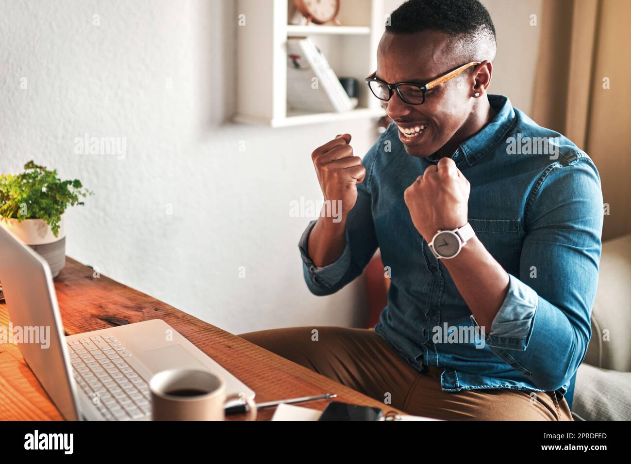 Creative entrepreneur with a laptop celebrating, cheering and feeling excited after reading email with good news. Happy, smiling and successful freelancer working from home on technology for startup Stock Photo