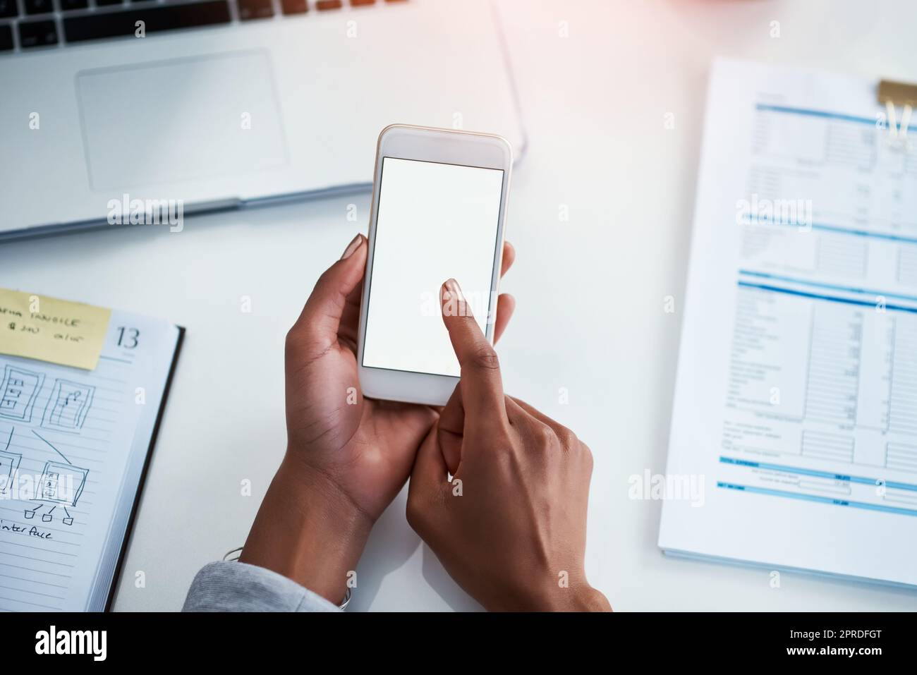 Phone in the hands of a business woman for communication, networking and calling from above. Female corporate professional typing a text message while sitting at a desk in a modern office with flare Stock Photo