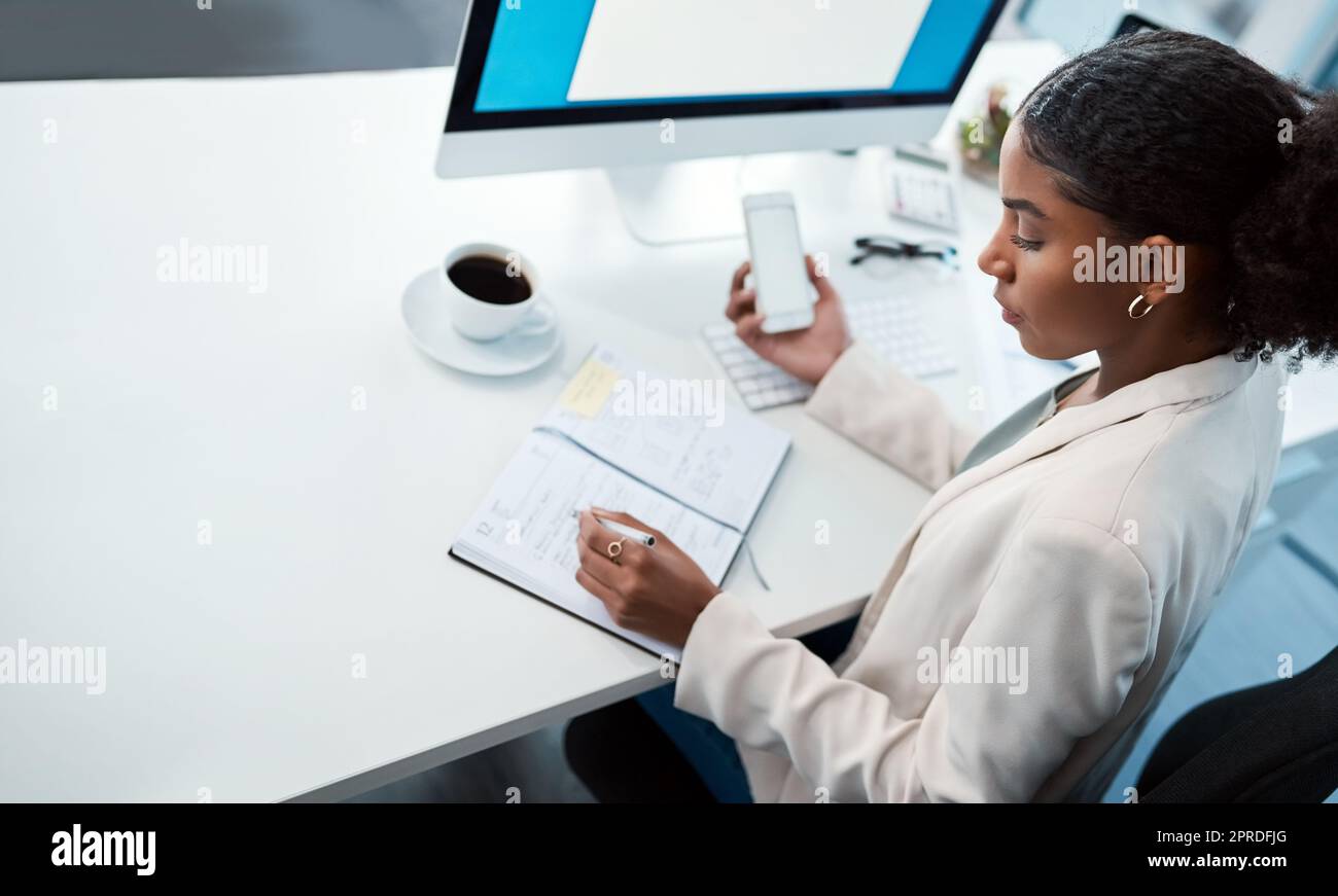 Entrepreneur, secretary and admin assistant holding phone while writing down appointments, schedule and business contacts at her desk. Professional woman doing online research and making notes Stock Photo