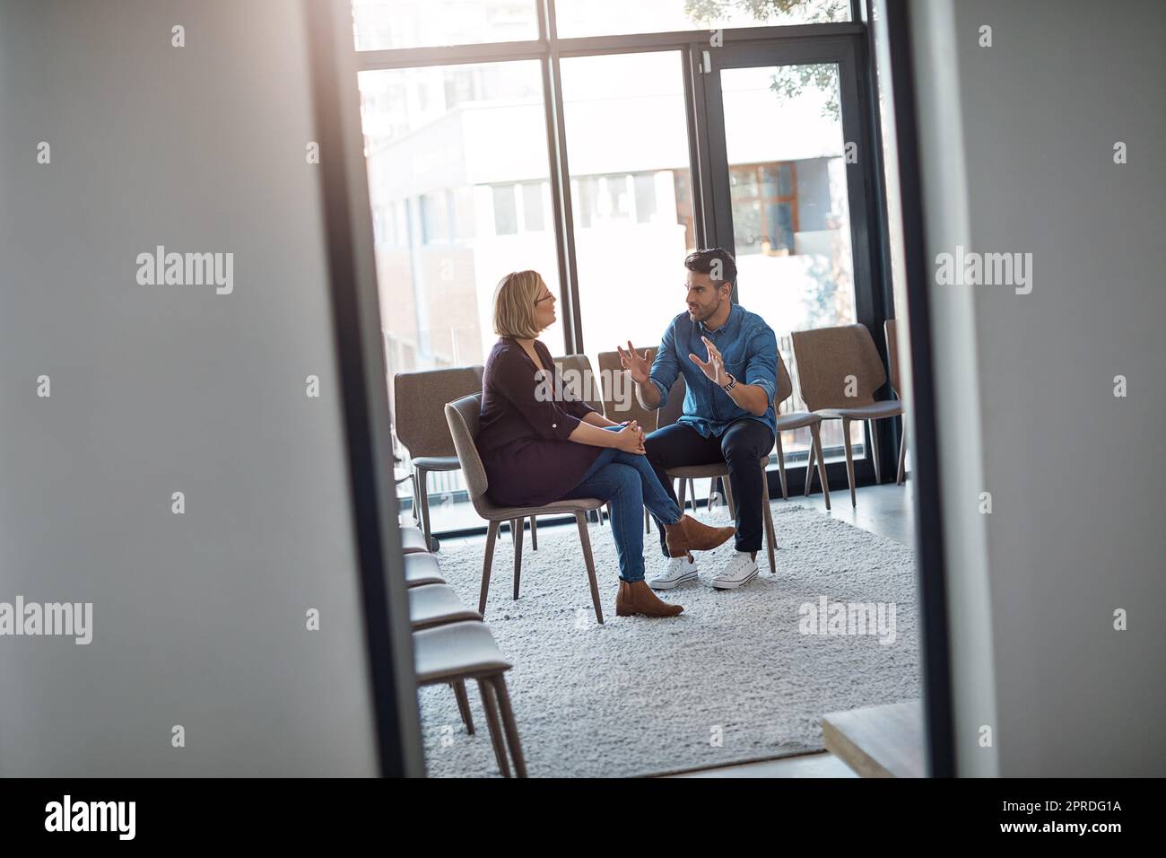 Young businessman talking to his therapist after a therapy meeting at a psychology office for mental health problems. Male employee having a discussion with a mature woman in a modern boardroom Stock Photo