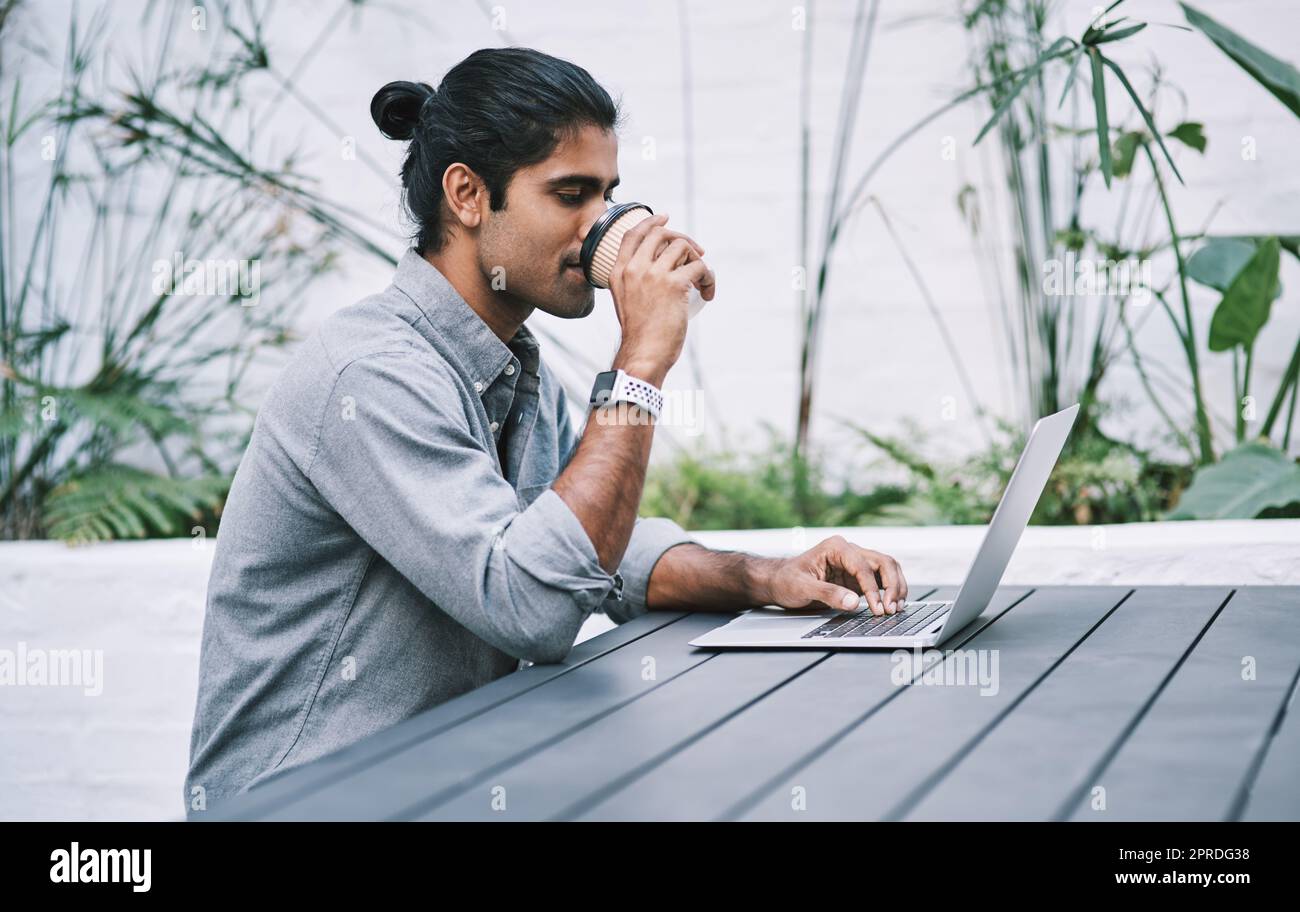 Coffee keeps those numbers up. a young businessman using a laptop and having coffee in a modern workplace. Stock Photo