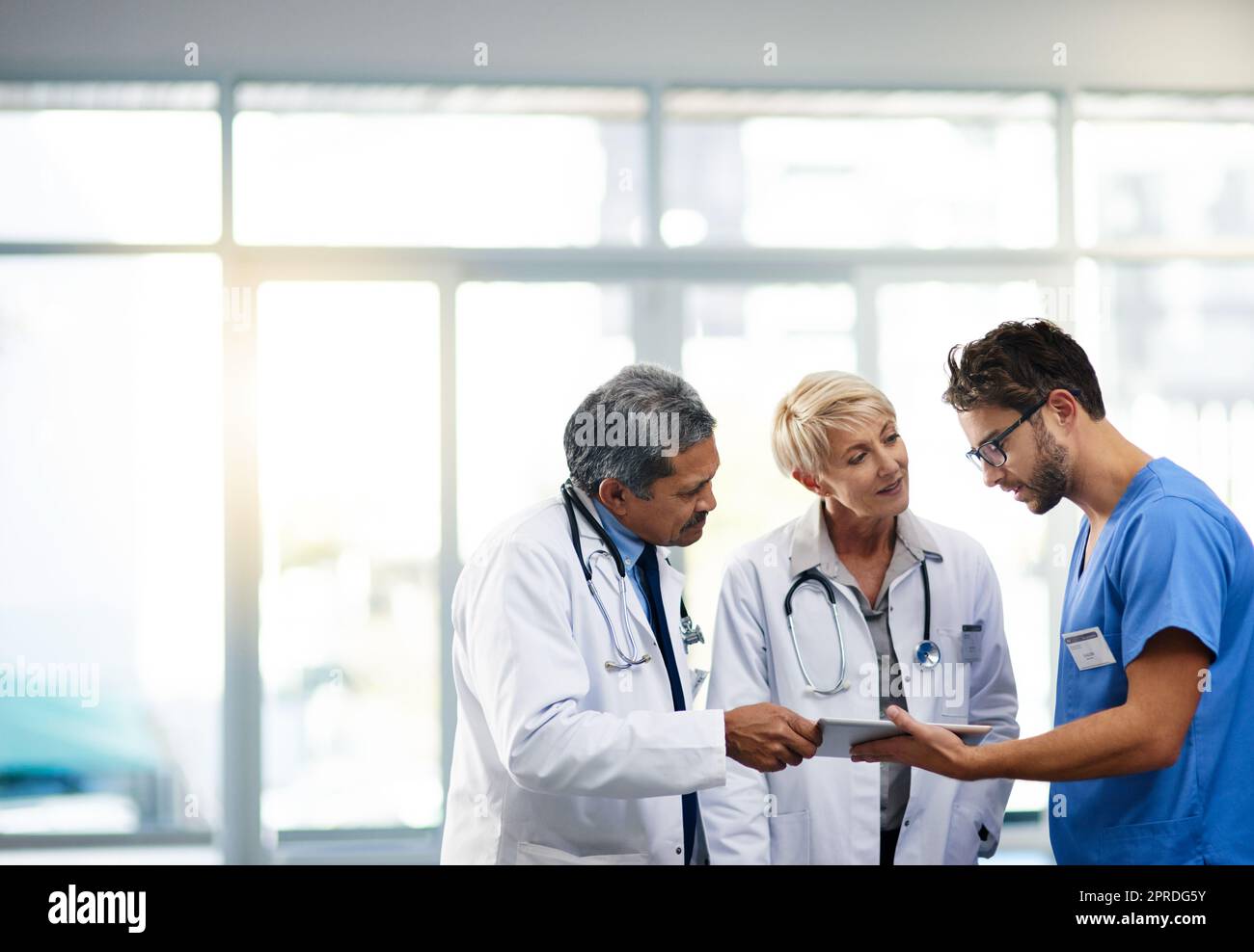 Medical professional, team and workers holding tablet, talking and solving a problem together online while standing at work in a hospital. Health experts discussing, planning and doing research Stock Photo