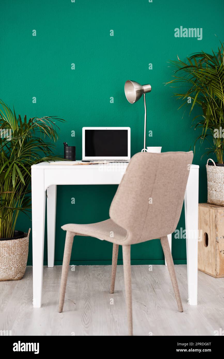 The space to get creative and productive. Still life shot of various items at a workstation against a green wall in an office. Stock Photo