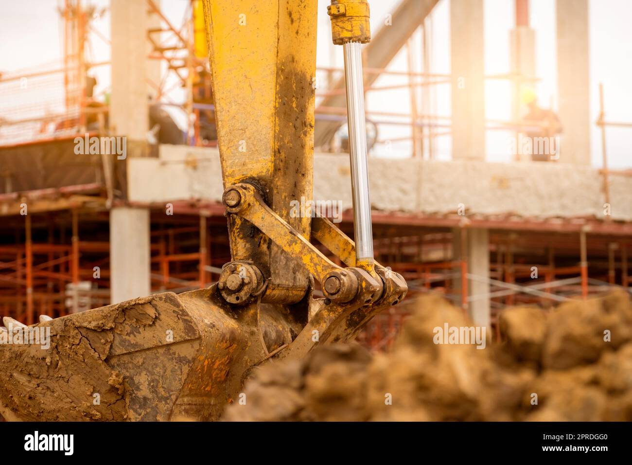 Bucket of backhoe. Digger parked at construction site. Bulldozer on blur building under construction and worker. Earth moving machine. Dirt bucket of digger. Earth moving machine. Excavation vehicle. Stock Photo