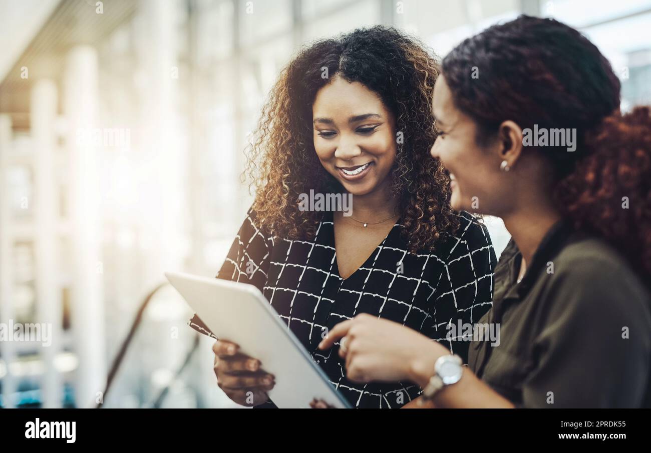 Our work will be so much easier with this tool. two attractive businesswomen using a digital tablet together while standing in a modern workplace. Stock Photo