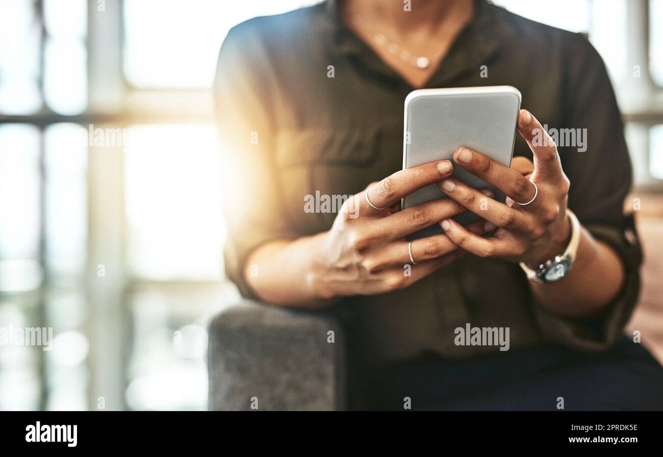 Let your mobile app schedule your plans for you. an unrecognizable businesswoman using a smartphone while sitting on a couch in a modern office. Stock Photo