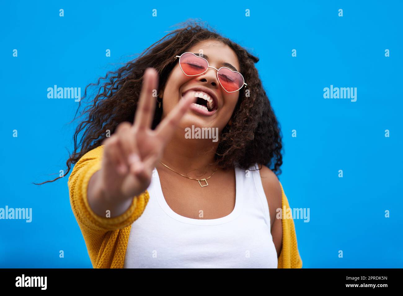 I choose peace and happiness. a young woman showing the peace sign against a blue background. Stock Photo