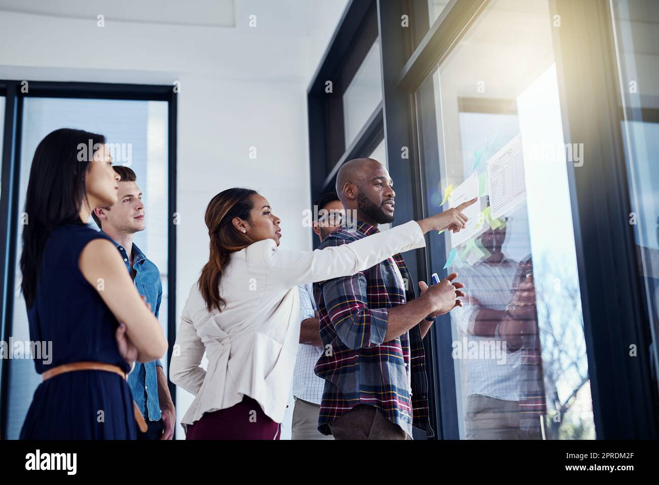 Hes got every point of interest covered. a young businesswoman giving a demonstration on a glass wall to her colleagues in a modern office. Stock Photo