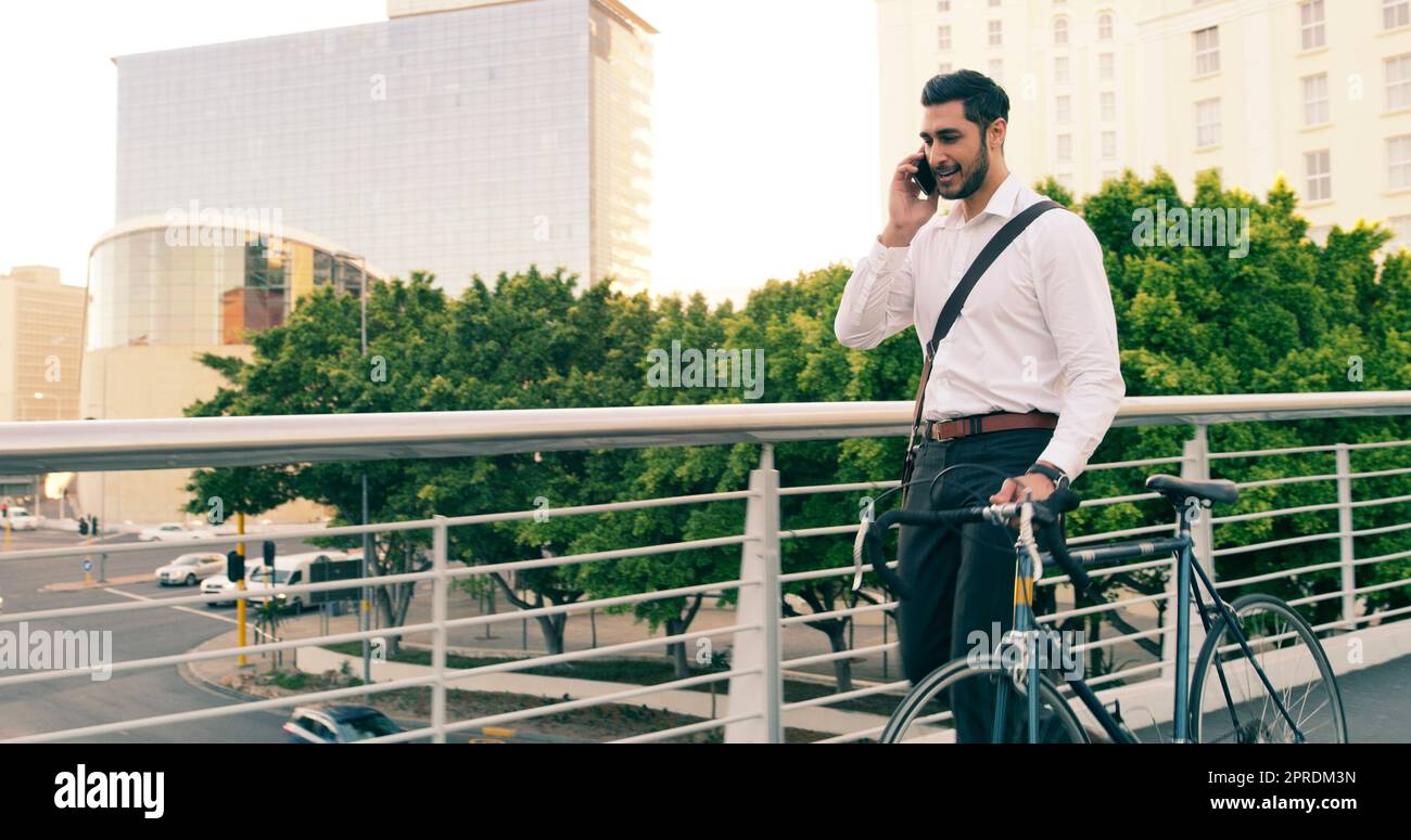 On route to success. a handsome young businessman taking a phone call while commuting to work with his bicycle. Stock Photo