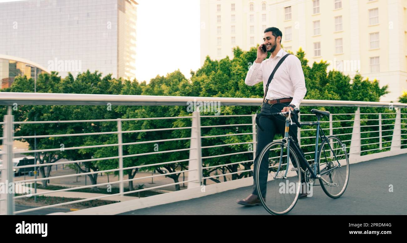 Focus on where youre headed, not where you come from. Full length shot of a handsome young businessman taking a phone call while commuting to work with his bicycle. Stock Photo