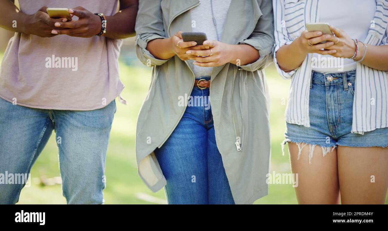 New age conversations. an unrecognizable group of friends each using their cellphones while standing in a park outdoors. Stock Photo