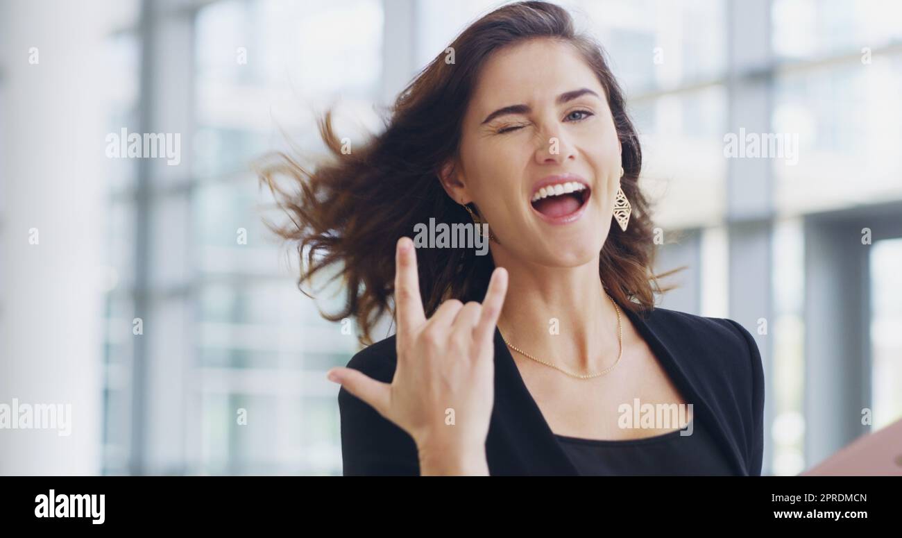 Im a rockstar in the business world. a young businesswoman showing a shaka hand sign while walking through a modern office. Stock Photo
