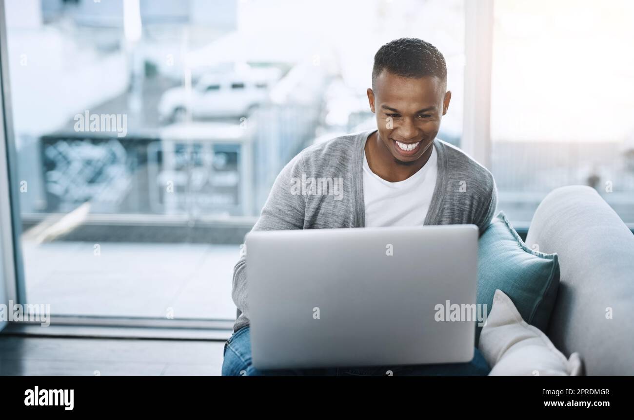 Social media is really buzzing today. a handsome young man using his laptop while sitting on a sofa at home. Stock Photo