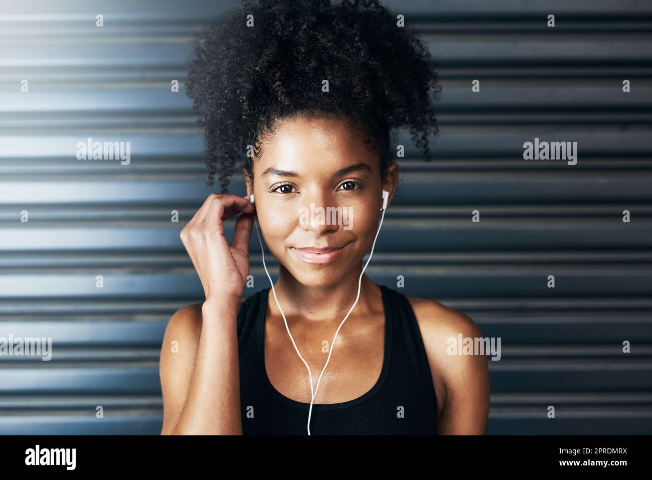 Lets go out for a heart-pumping run. Portrait of a sporty young woman listening to music while exercising against a grey background. Stock Photo