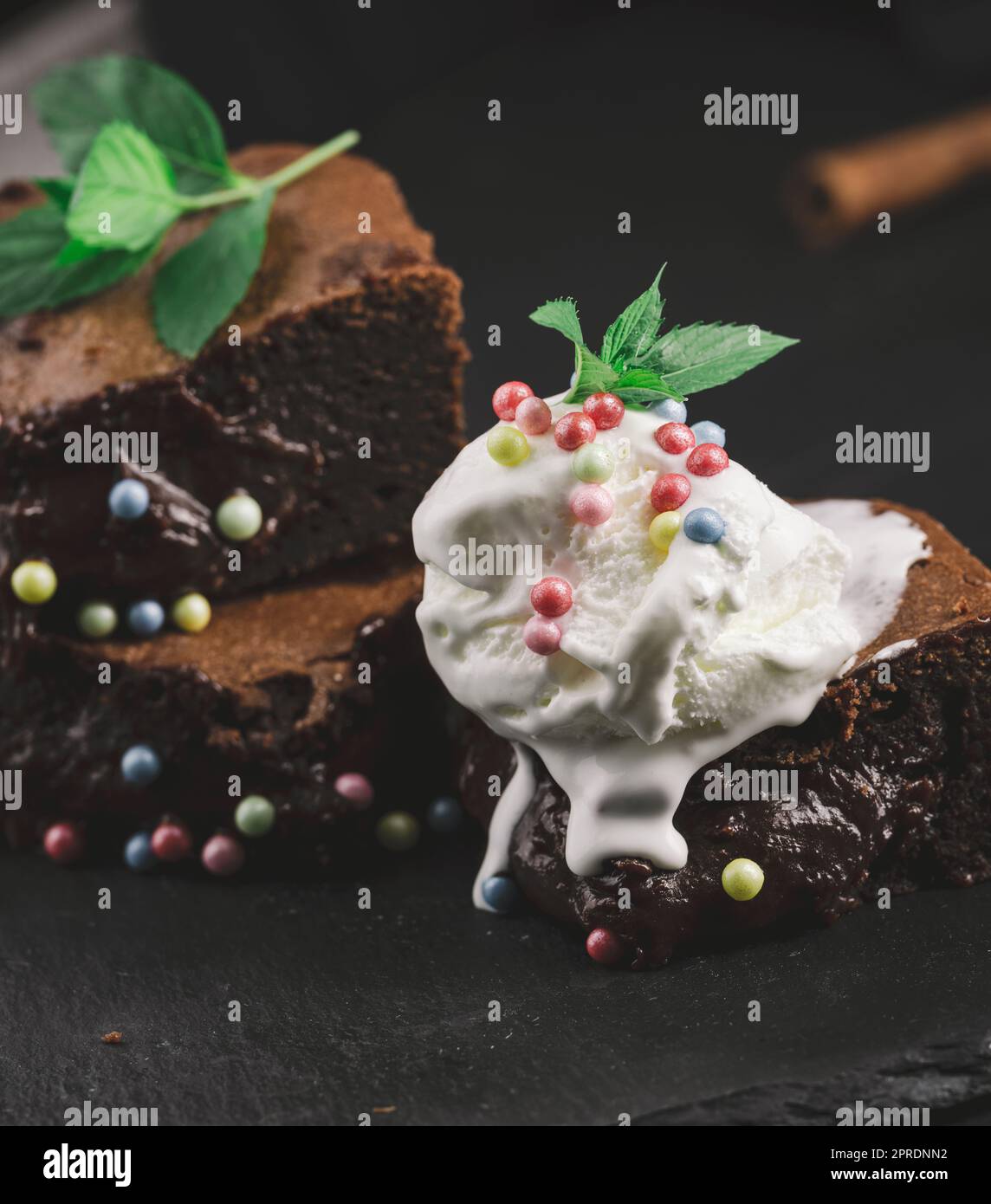 Baked pieces of chocolate brownie pie on a black table, on top of a scoop of ice cream Stock Photo