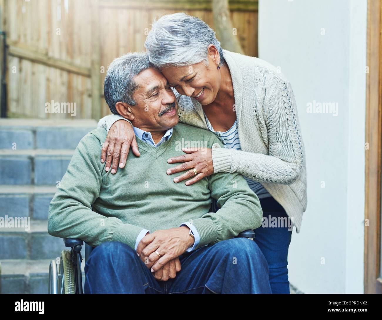 Im so blessed to have you in my life. a cheerful elderly man seated in a wheelchair while being held by his loving wife outside at home during the day. Stock Photo