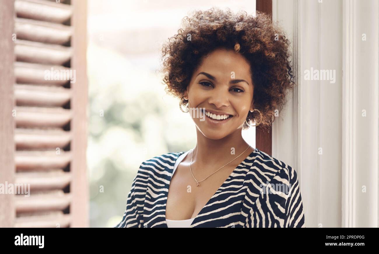 Beautiful, happy and edgy african woman smiling and showing a positive attitude while standing alone. Portrait of attractive black female with curly afro and friendly attitude while relaxing at home Stock Photo