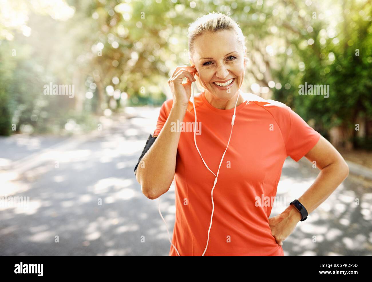 Fit female athlete going for morning run, adjusting earphones, listening to music. Happy, healthy sports woman smiling, about to do cardio wellness exercise or take endurance training workout break. Stock Photo