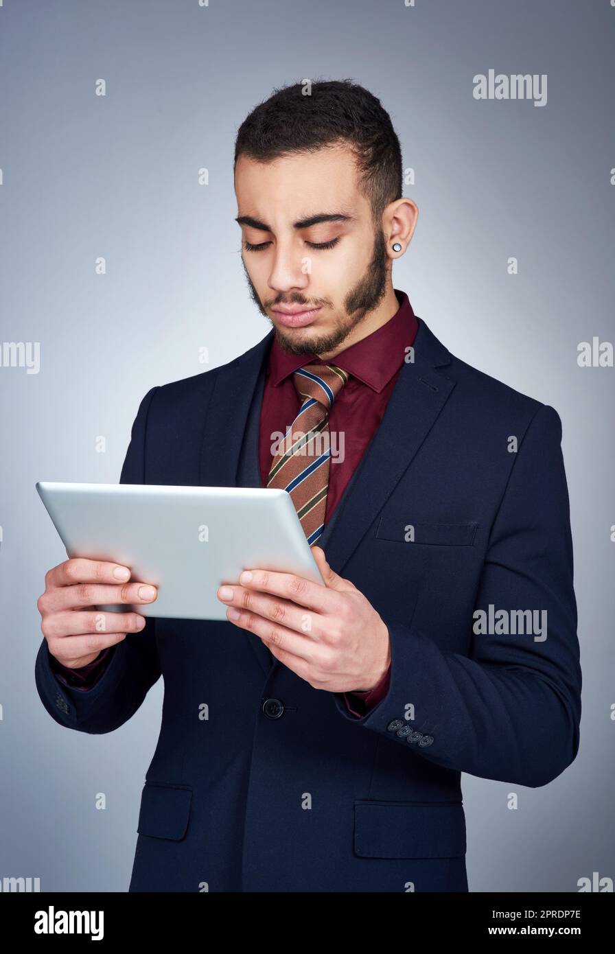 Technology can be a helpful tool in business. Studio shot of a handsome young businessman using a tablet against a grey background. Stock Photo