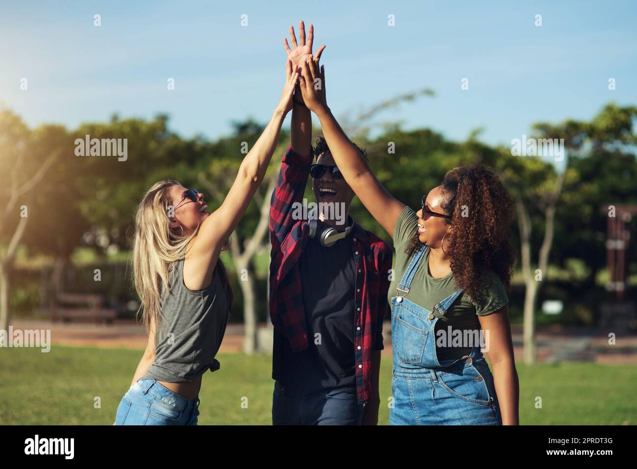 Lets get this day started. a group of cheerful young friends giving each other high fives outside in a park. Stock Photo