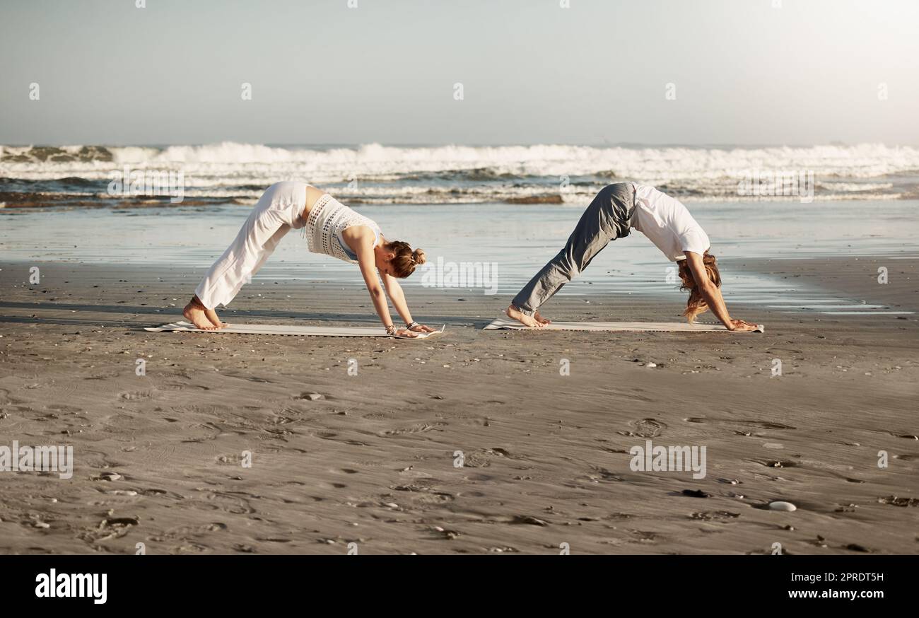 It is through yoga we gain strength and find peace. a young couple practising yoga together on the beach. Stock Photo