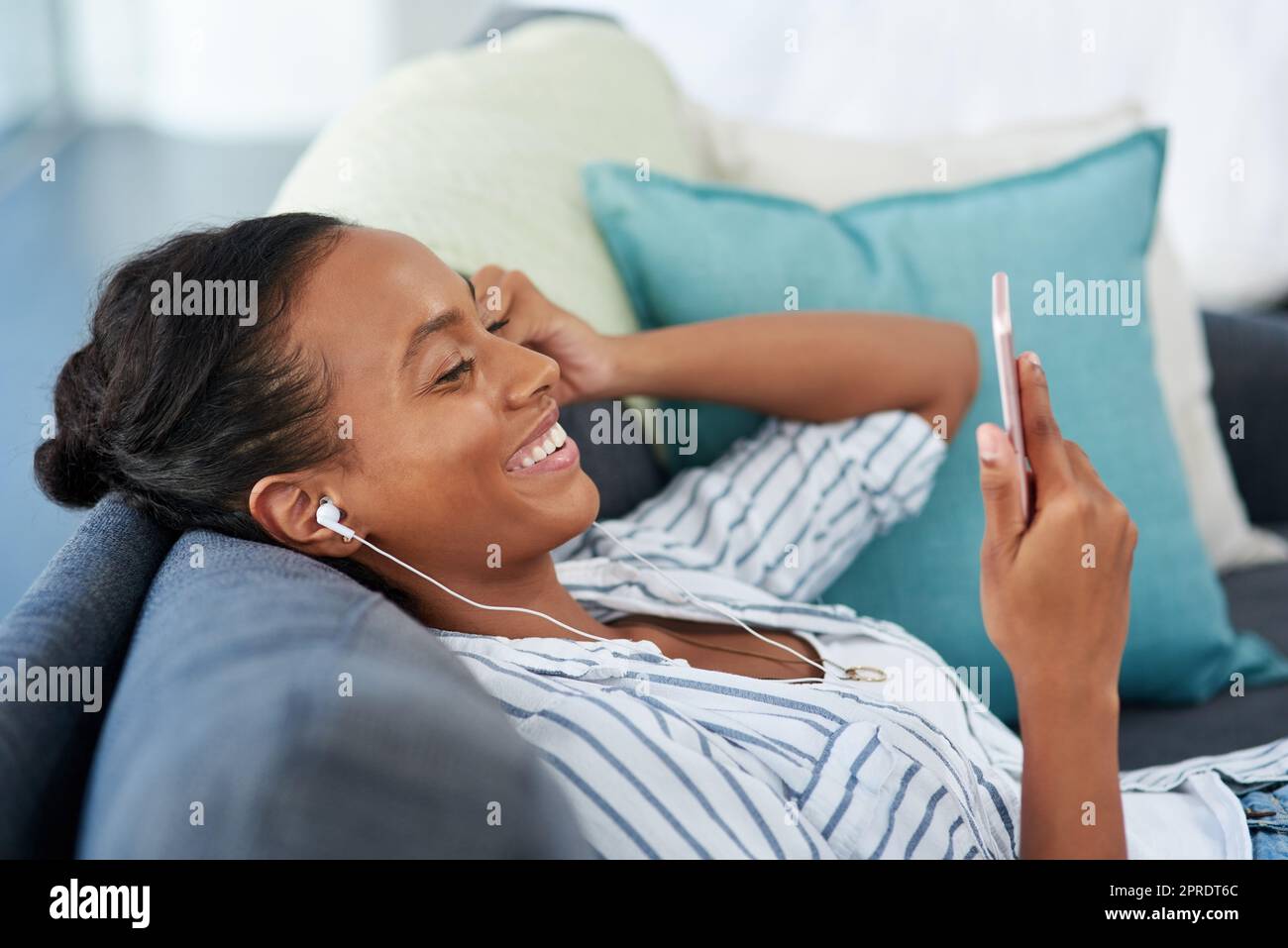 Plugged in to her weekend jams. a young woman wearing earphones while using a cellphone at home. Stock Photo