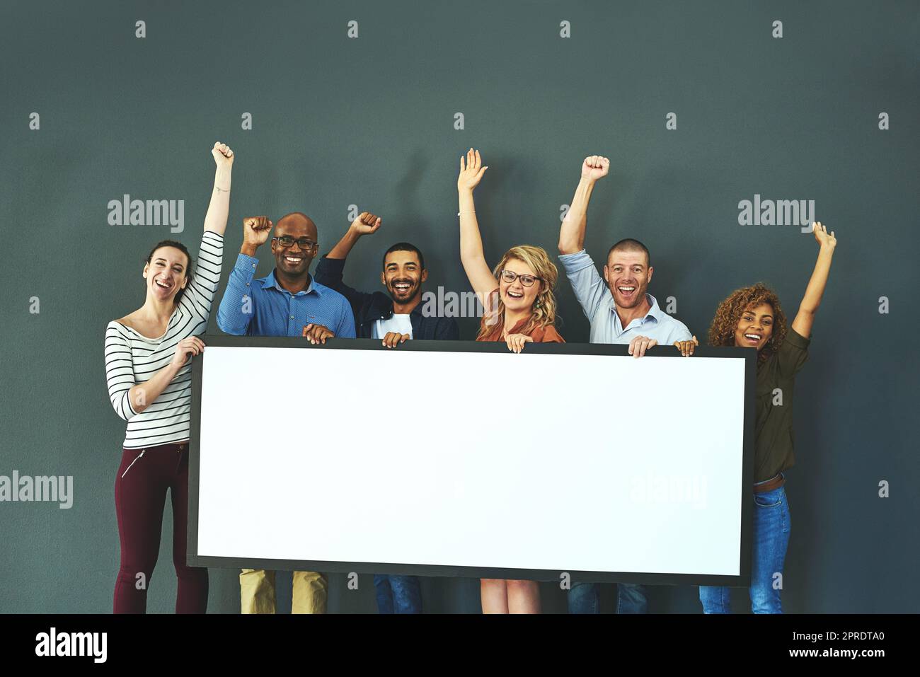 Happy, diverse and cheering marketing team with a blank card, poster or billboard with copyspace in studio on a grey background. A group of smiling business people celebrating and endorsing a product Stock Photo