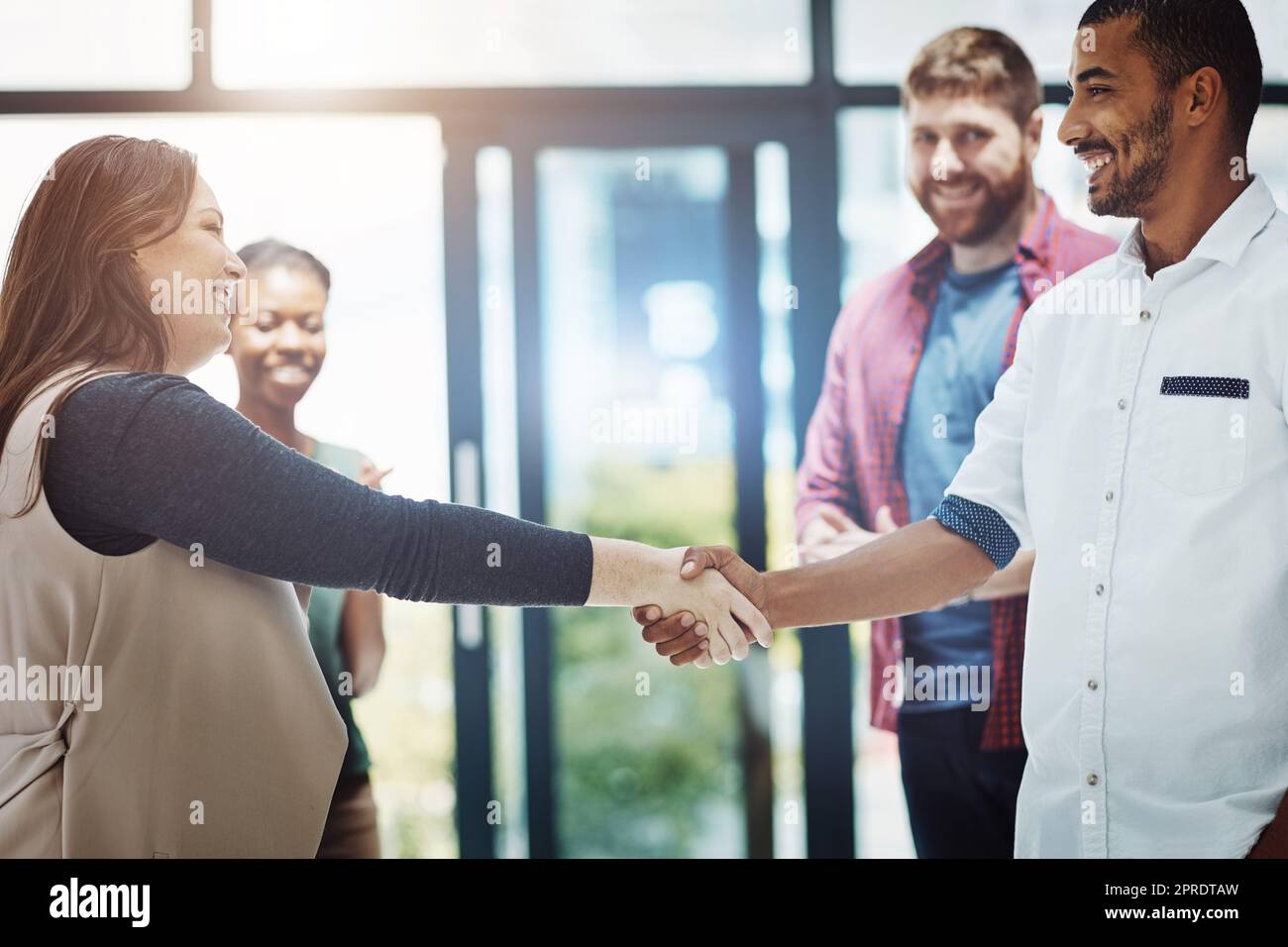 Business people giving handshake, welcoming new employee and standing united while colleagues clap in meeting at work. Coworkers shaking hands, celebrating success or congratulating on a promotion Stock Photo