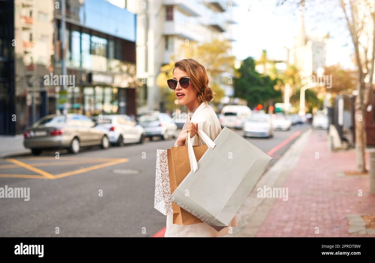 Stylish fashion model shopping in the city and walking outdoors with bags. Young, edgy and carefree female with an expensive lifestyle standing in the street with bags in an urban town Stock Photo