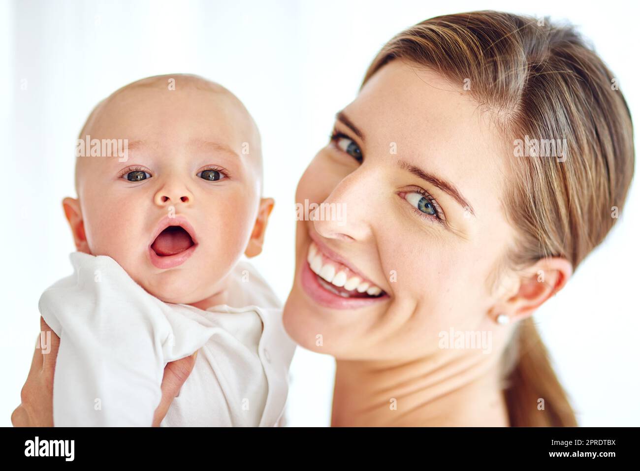Cute, adorable baby bonding with mother enjoying quality playtime together at home. Proud, loving and happy woman holding her little newborn child while bonding together against a white background Stock Photo